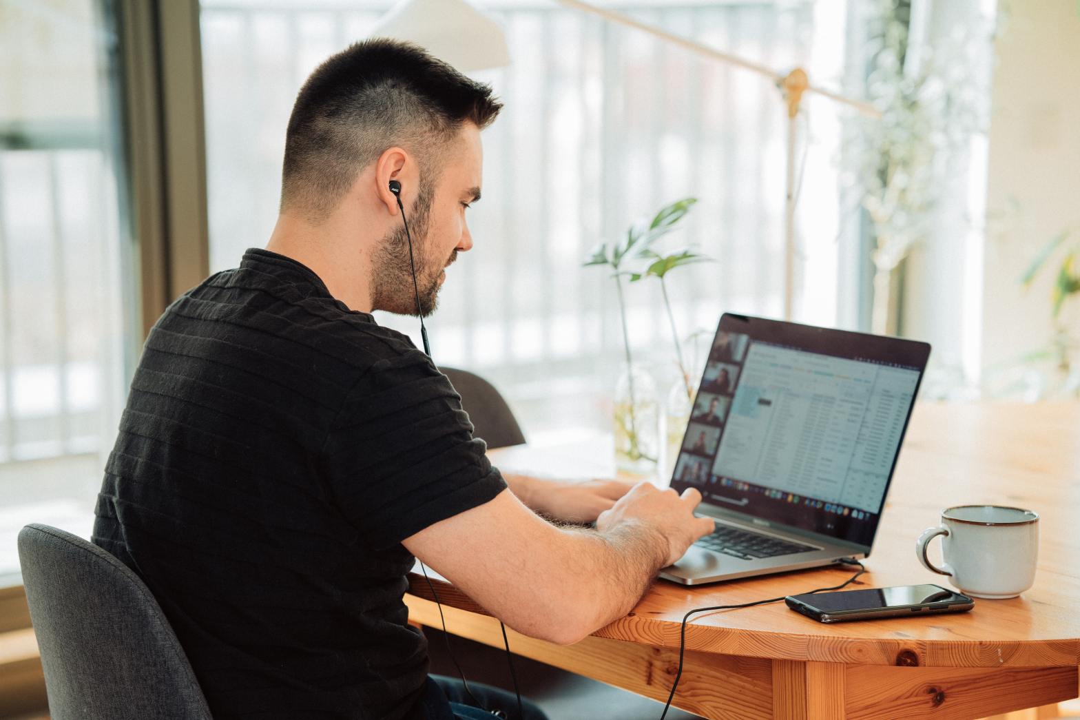 Uma foto colorida feita em ambiente interno. Mostra um homem sentado em uma mesa de trabalho, teclando em um notebook.